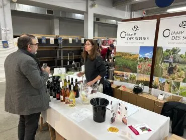 stand de vin avec une femme vigneron qui parle avec un visiteur, verre à la main